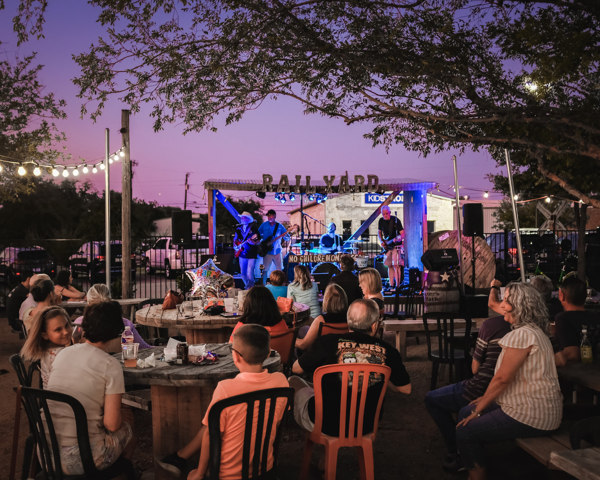 A crowd sitting at tables enjoys outdoor live music at the Frisco Rail Yard.