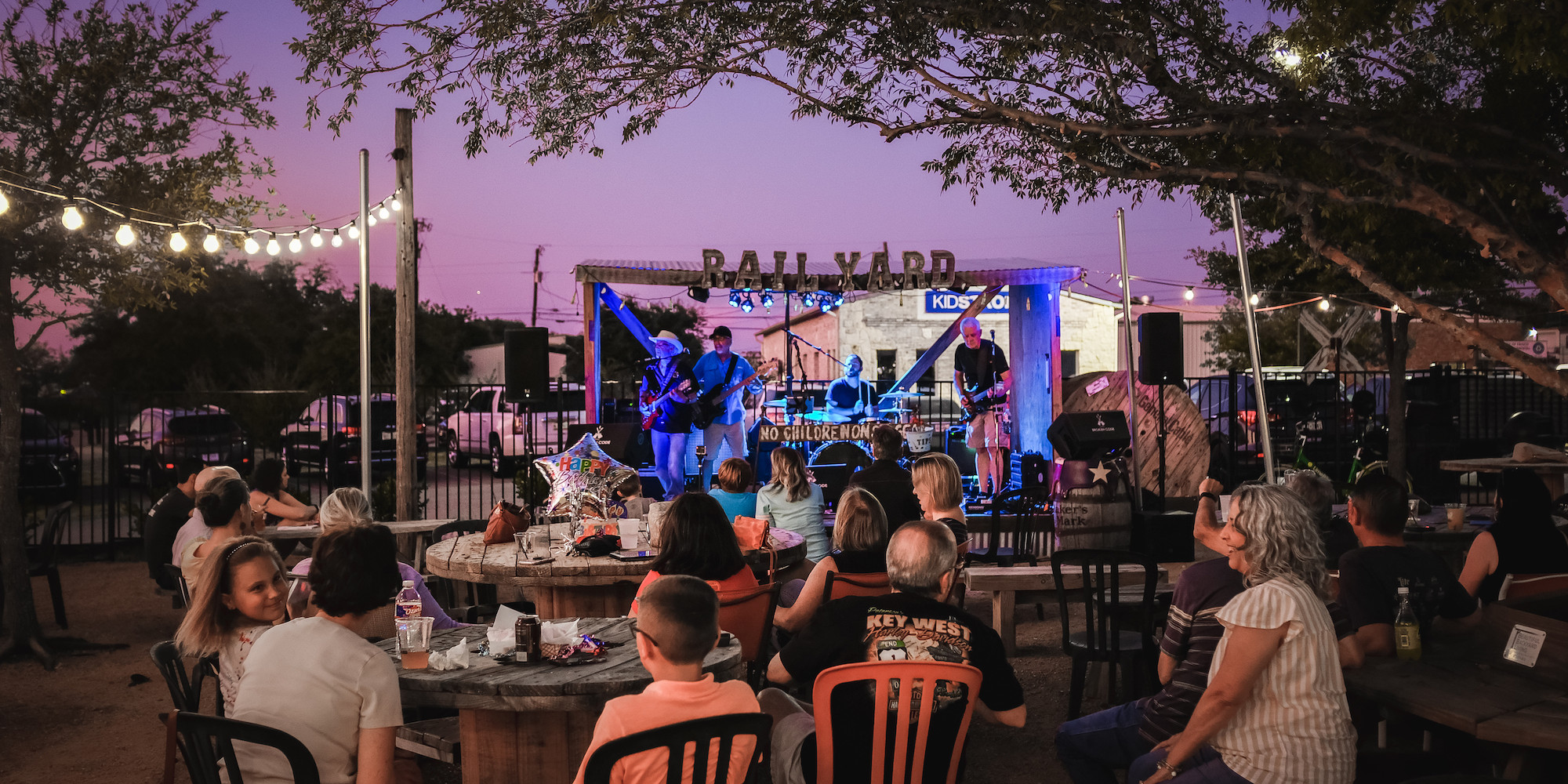 A crowd sitting at tables enjoys outdoor live music at the Frisco Rail Yard.