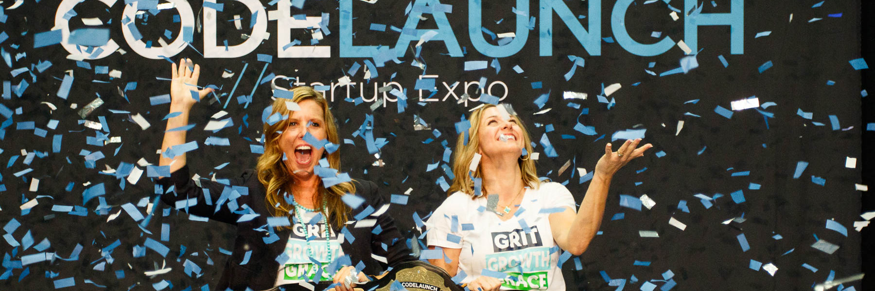 Two ladies on stage smile as blue confetti falls at Code Launch.