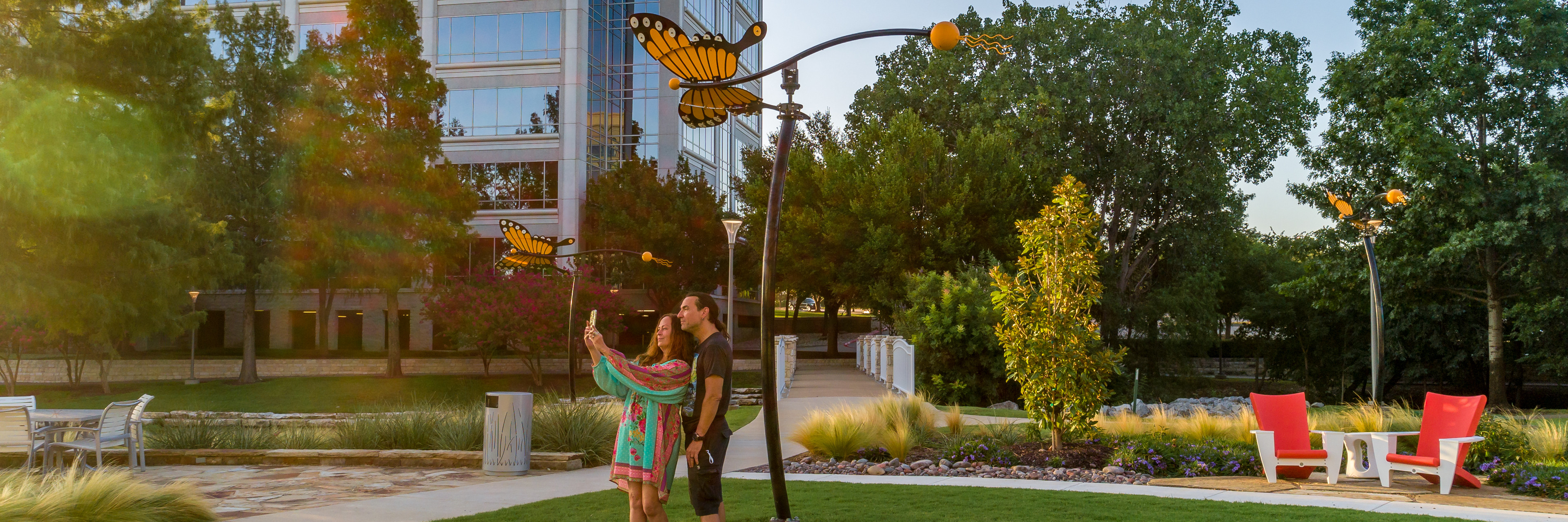 Two people stand in the grass taking a selfie in the Texas Sculpture Garden located in Hall Park.