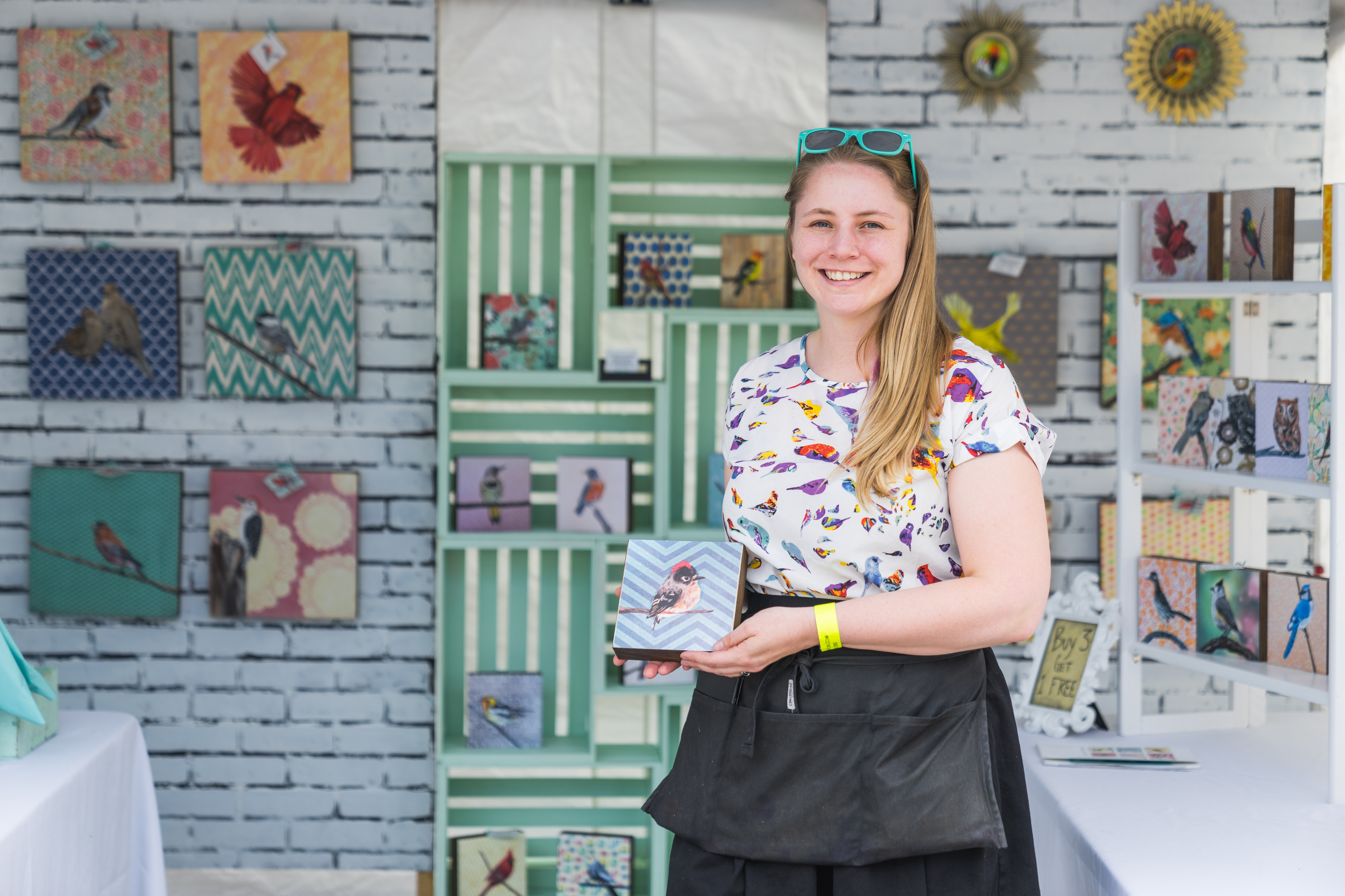 An artists holds her small painting of a bird and smiles for a picture.