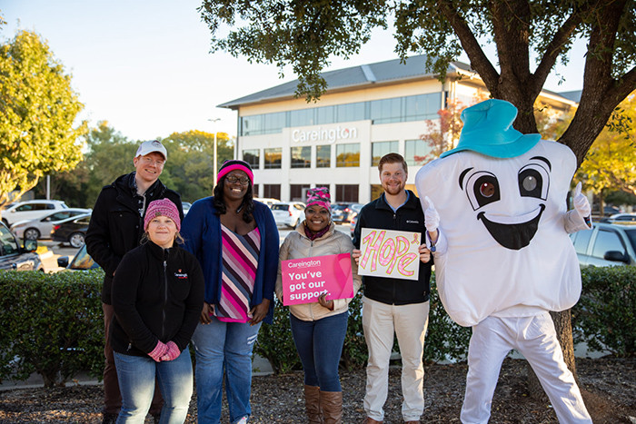 Five Careington employees gather outside the Careington building with a person dressed in a tooth costume.