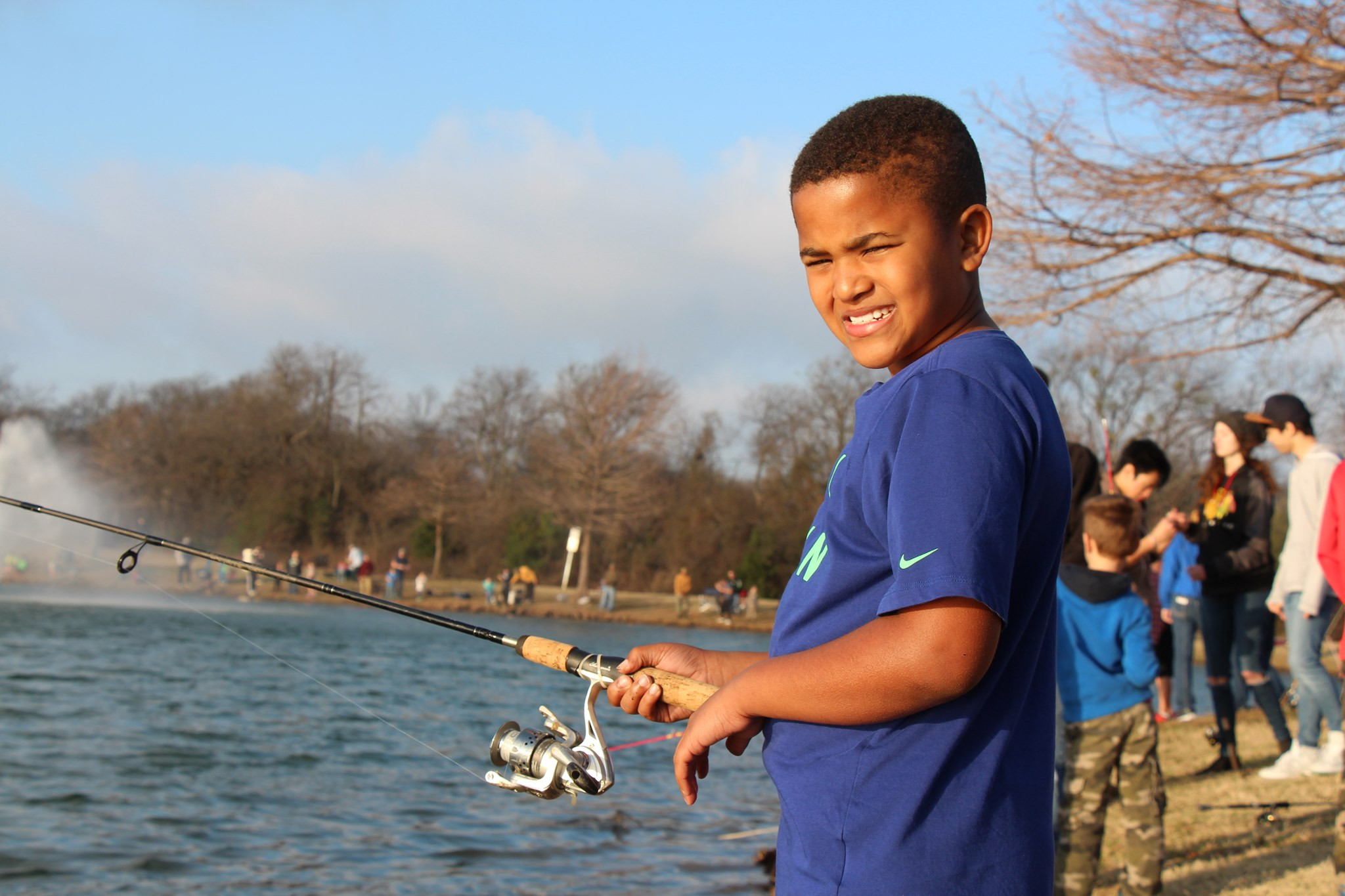 A child poses at a pond with his fishing reel.