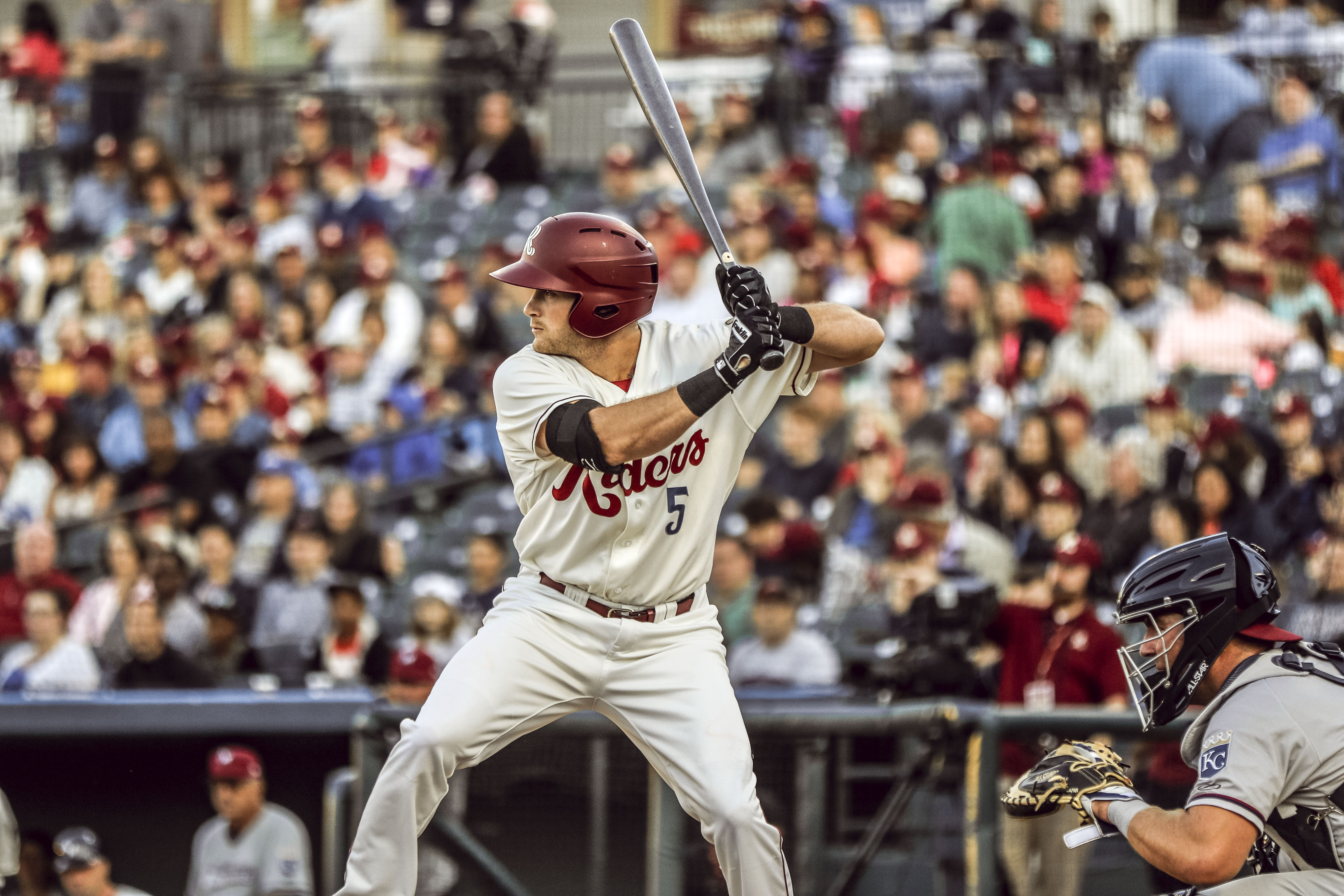 A Frisco RoughRiders batter is up to bat. The crowd of full seats is in the background.