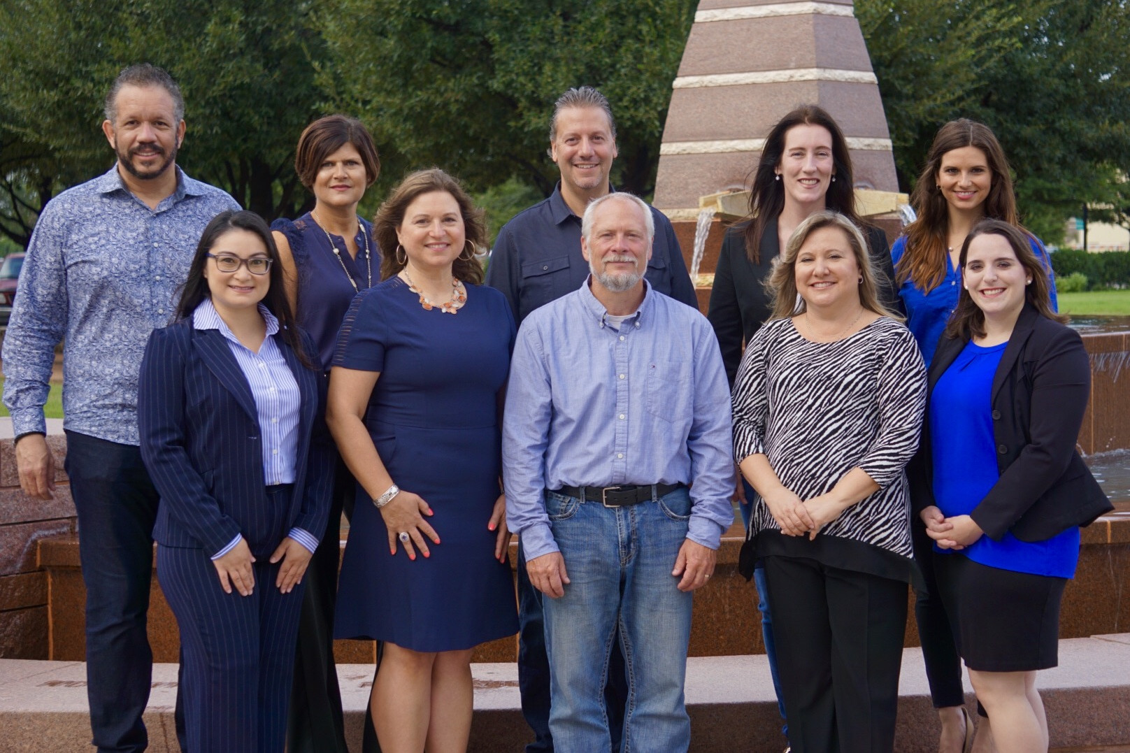 A group of 10 H Architect employees in 2 rows post for a photo. They wear a variety of blue and black clothing.