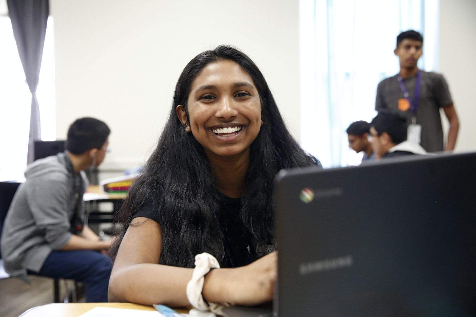 A student sits at their laptop and smiles for a photo.
